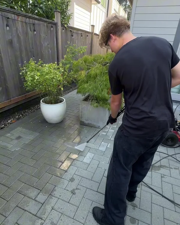 West Wave Wash field technician pressure washing an interlocking paver surface with a visible clean line
